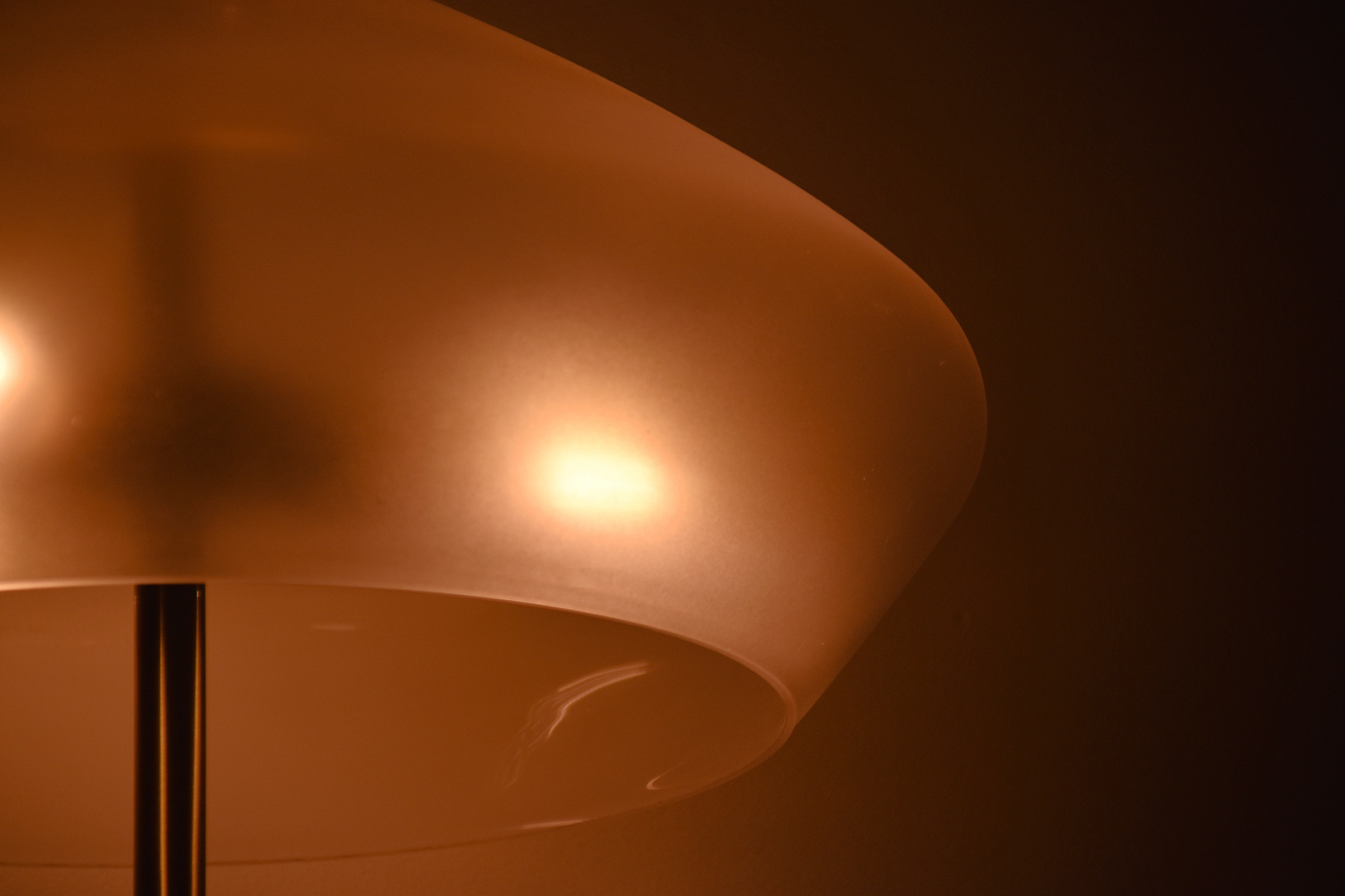 A frosted glass lamp shade glowing amber in a dark room, the bulb showing softly through the diffuser.